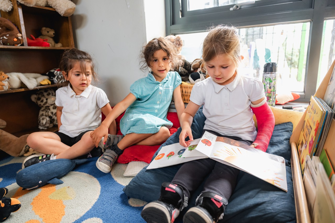 Three children sitting in the reading corner sharing a story Three children reading a book together
