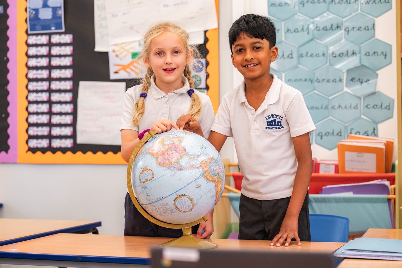 Two children smiling at the camera with a globe on the desk in front of them Two children smiling at the camera with a globe on the desk in front of them