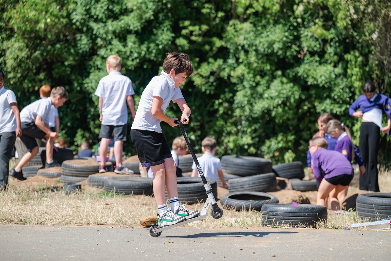 A child playing on a scooter with children moving tyres in the background