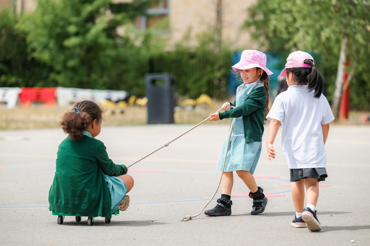 A child pulling another on a wheeled object using a rope